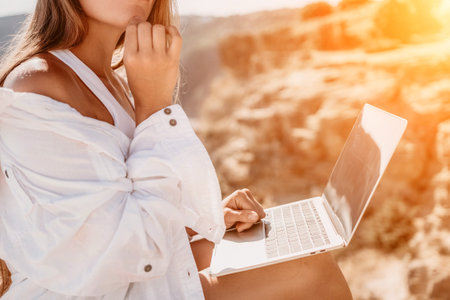 Woman sea laptop. Business woman in yellow hat freelancer with laptop working over blue sea beach. Girl relieves stress from work. Freelance, digital nomad, travel and holidays conceptの写真素材
