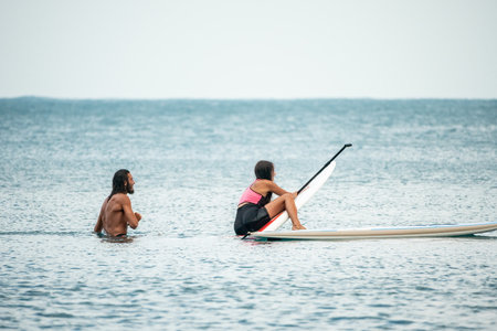 Sea woman and man on sup. Silhouette of happy young woman and man, surfing on SUP board, confident paddling through water surface. Idyllic sunset. Active lifestyle at sea or river.の写真素材