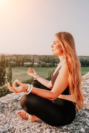 Fitness woman. Well looking middle aged woman with long hair, fitness instructor in leggings and tops doing stretching and pilates on the rock near forest. Female fitness yoga routine concept.の写真素材
