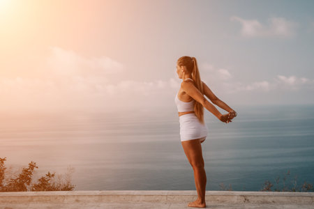 Fitness woman sea. A happy middle aged woman in white sportswear exercises morning outdoors in a park with a beach view. Female fitness pilates yoga routine concept. Healthy lifestyle.の写真素材