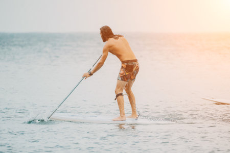 Sea woman and man on sup. Silhouette of happy young woman and man, surfing on SUP board, confident paddling through water surface. Idyllic sunset. Active lifestyle at sea or river.の写真素材