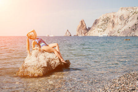 Woman travel sea. Happy tourist in blue swimwear takes a photo outdoors to capture memories. woman traveling and enjoying her surroundings on the beach, with volcanic mountains in the background.の写真素材