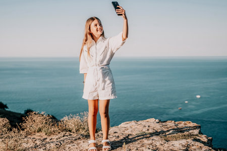 Woman travel sea. Happy tourist in hat enjoy taking picture outdoors for memories. Woman traveler posing on the beach at sea surrounded by volcanic mountains, sharing travel adventure journeyの写真素材