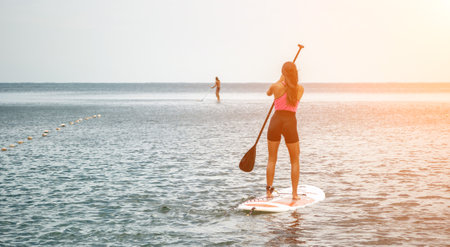 Sea woman and man on sup. Silhouette of happy young woman and man, surfing on SUP board, confident paddling through water surface. Idyllic sunset. Active lifestyle at sea or river.の写真素材