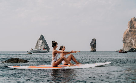 Woman sup yoga. Happy sporty woman practising yoga pilates on paddle sup surfboard. Female stretching doing workout on sea water. Modern individual female hipster outdoor summer sport activity.の写真素材