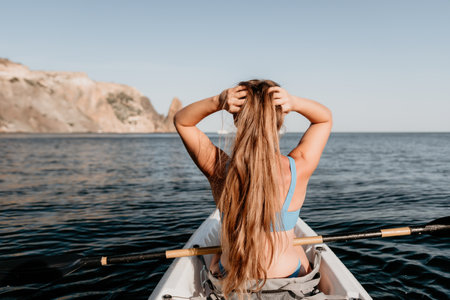Woman in kayak back view. Happy young woman with long hair floating in kayak on calm sea. Summer holiday vacation and cheerful female people relaxing having fun on the boat.の写真素材