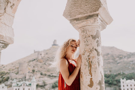Redhead woman portrait. Curly redhead young caucasian woman with freckles looking at camera and smiling. Cute woman close up portrait in a red long dress posing on sea and travel city backgroundの写真素材