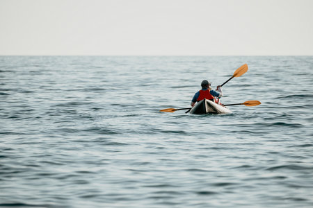 Happy couple kayaks in an inflatable kayak on the sea at sunset. Couple kanoeing in the sea near the island with mountains. People kayaking in life jackets sail. Back viewの写真素材