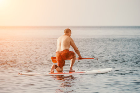 Active mature male paddler with his paddleboard and paddle on a sea at summer. Happy senior man stands with a SUP board. Stand up paddle boarding - outdor active recreation in nature.の写真素材