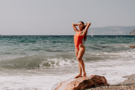 Woman summer travel sea. Happy tourist in red bikini enjoy taking picture outdoors for memories. Woman traveler posing on beach at sea surrounded by volcanic mountains, sharing travel adventure joyの写真素材