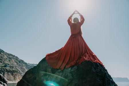 Woman travel sea. Young Happy woman in a long red dress posing on a beach near the sea on background of volcanic rocks, like in Iceland, sharing travel adventure journeyの写真素材
