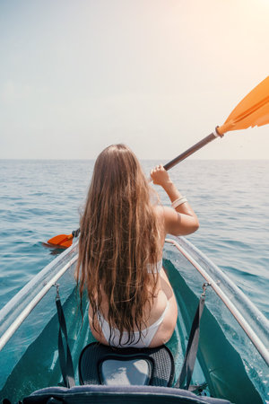 Woman in kayak back view. Happy young woman with long hair floating in transparent kayak on the crystal clear sea. Summer holiday vacation and cheerful female people relaxing having fun on the boatの写真素材