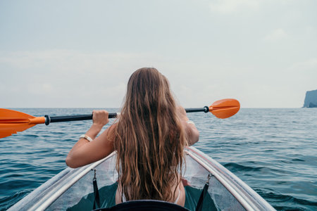 Woman in kayak back view. Happy young woman with long hair floating in transparent kayak on the crystal clear sea. Summer holiday vacation and cheerful female people relaxing having fun on the boatの写真素材