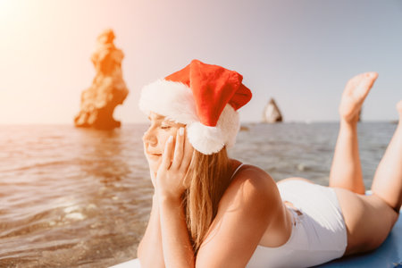 Woman sea sup. Close up portrait of happy young caucasian woman with long hair in Santa hat looking at camera and smiling. Cute woman portrait in a white bikini posing on sup board in the seaの写真素材