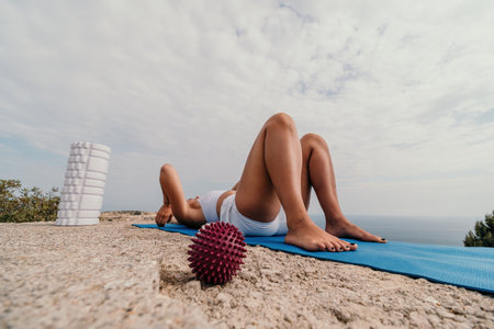 Woman sea pilates. Sporty happy middle-aged woman practices pilates on a beach near the sea, promoting a healthy lifestyle through outdoor fitness and meditation.の写真素材