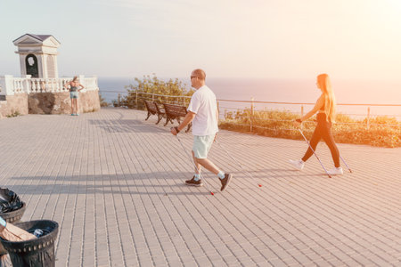 Happy Middle aged couple or friends practicing nordic walking in park near sea. Mature couple with...