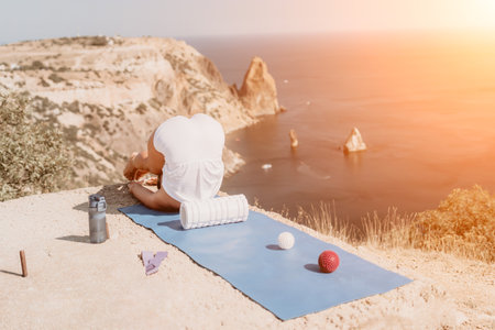 Woman sea pilates. Sporty happy middle aged woman practicing fitness on yoga mat with balls and roller near sea, smiling active female outside, enjoying healthy lifestyle, harmony and meditation.の写真素材