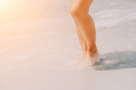 Sea beach travel - woman walking on sand beach leaving footprints in the white sand. Female legs walking along the seaside barefoot, close-up of the tanned legs of a girl coming out of the water.の写真素材