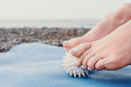Woman sea yoga. Well looking middle aged woman with braids dreadlocks in white leggings and tops doing stretching pilates on yoga mat near sea. Female fitness yoga routine concept. Healthy lifestyle.の写真素材