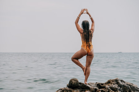 Woman sea yoga. Back view of free calm bliss satisfied woman with long hair standing on top rock with yoga position against of sky by the sea. Healthy lifestyle outdoors in nature, fitness concept.の写真素材