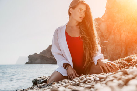 Young woman in red bikini on Beach. Girl lying on pebble beach and enjoying sun. Happy lady with long hair in bathing suit chilling and sunbathing by turquoise sea ocean on hot summer day. Close upの写真素材