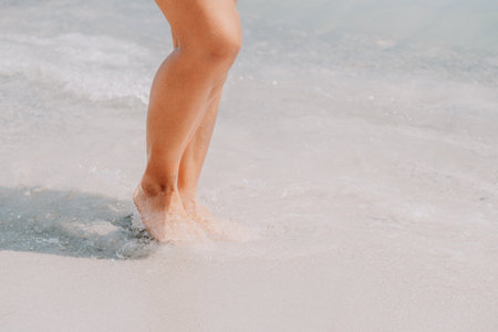 Sea beach travel - woman walking on sand beach leaving footprints in the white sand. Female legs walking along the seaside barefoot, close-up of the tanned legs of a girl coming out of the water.の写真素材