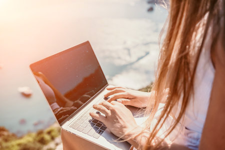 Digital nomad, woman in the hat, a business woman with a laptop sits on the rocks by the sea during...