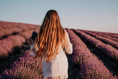 Woman lavender field. Happy carefree woman in a white dress walking in a lavender field and smelling a lavender bouquet on sunset. Ideal for warm and inspirational concepts in wanderlust and travel.の写真素材