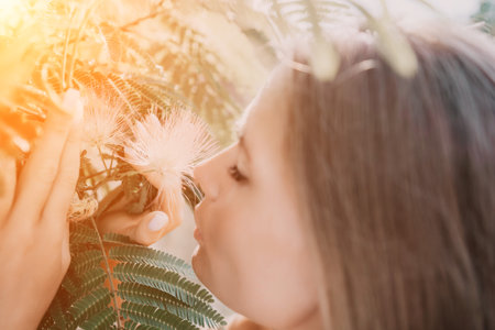 Beauty portrait of happy woman closeup. Young girl smelling Chinese acacia pink blossoming flowers. Portrait of young woman in blooming spring, summer garden. Romantic vibe. Female and natureの写真素材