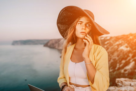 Digital nomad, Business woman working on laptop by the sea. Pretty lady typing on computer by the sea at sunset, makes a business transaction online from a distance. Freelance, remote work on vacationの写真素材