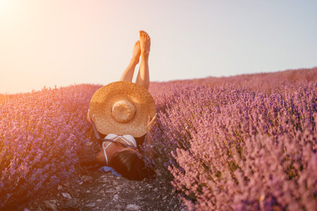 Woman lavender field. Happy carefree Woman legs stick out of the lavender bushes, warm sunset light. Bushes of lavender purple in blossom, aromatic flowers at lavender fields.の写真素材