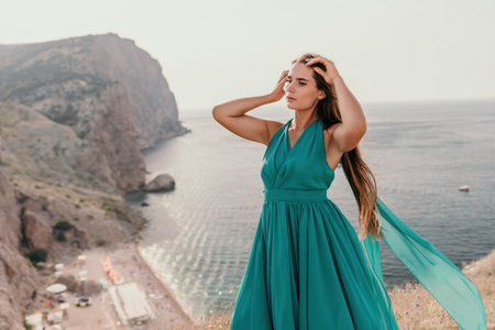 Woman travel portrait. Happy woman with long hair looking at camera and smiling. Close up portrait cute woman in a mint long dress posing on a volcanic rock high above the seaの写真素材