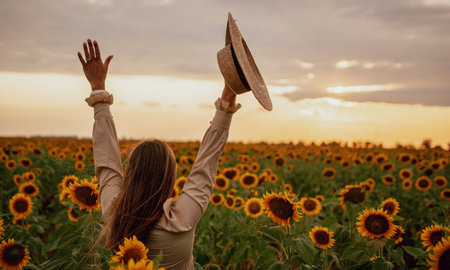 Woman in Sunflower Field: Happy girl in a straw hat stands in a vast field of sunflowers at sunset. Summer time.の写真素材