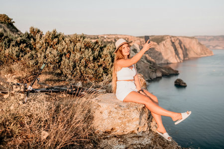 Woman travel sea. Happy tourist in hat enjoy taking picture outdoors for memories. Woman traveler posing on the beach at sea surrounded by volcanic mountains, sharing travel adventure journeyの写真素材