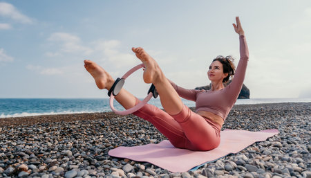 Woman sea pilates. Sporty happy middle aged woman practicing fitness on beach near sea, smiling active female training with ring on yoga mat outside, enjoying healthy lifestyle, harmony and meditationの写真素材