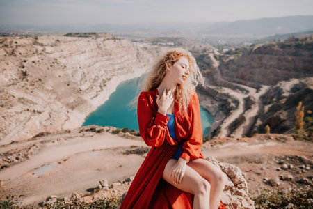 Close up portrait of curly redhead young caucasian woman with freckles looking at camera and smiling. Cute woman portrait in a pink long dress posing on a volcanic rock high above the sea at sunsetの写真素材