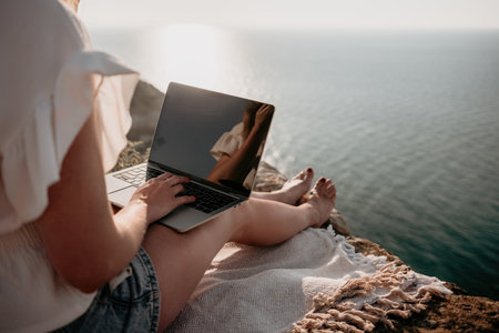 Woman sea laptop. Business woman working on laptop by sea at sunset. Close up on hands of pretty...