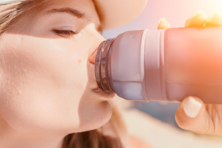Fintess woman drinking water. Happy, active middle aged woman standing on beach and drinking water...