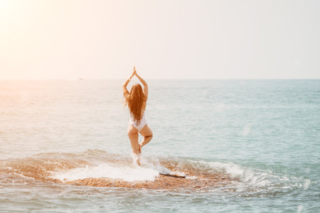 Woman sea yoga. Back view of free calm happy satisfied woman with long hair standing on top rock with yoga position against of sky by the sea. Healthy lifestyle outdoors in nature, fitness conceptの写真素材