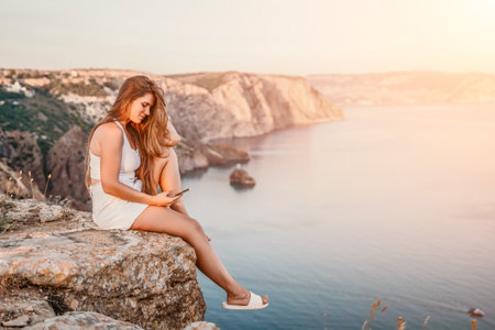 Woman travel sea. Happy tourist in hat enjoy taking picture outdoors for memories. Woman traveler posing on the beach at sea surrounded by volcanic mountains, sharing travel adventure journeyの写真素材