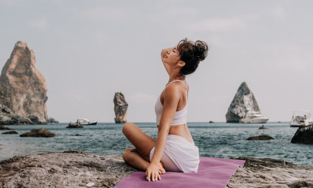 Fitness woman sea. A happy middle aged woman in white sportswear exercises morning outdoors on a beach with volcanic rocks by the sea. Female fitness pilates yoga routine concept. Healthy lifestyle.の写真素材