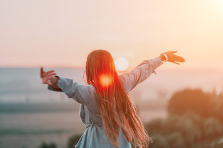 Happy woman standing with her back on the sunset in nature in summer with open hands. Romantic beautiful bride in white boho dress posing with mountains on sunsetの写真素材