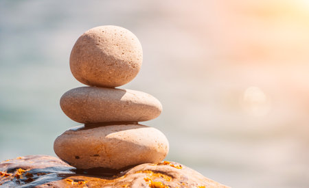 Balanced rock pyramid on sea pebbles beach, sunny day and clear sky at sunset. Golden sea bokeh on background. Selective focus, zen stones on sea beach, meditation, spa, harmony, calm, balance conceptの写真素材