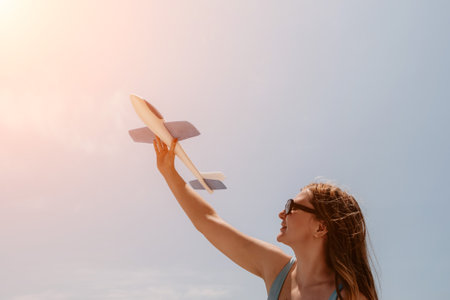 Woman hand holding toy airplane on blue sky and white clouds at seaside, dream of travel by plane. Happy woman has fun in summer vacation by sea and mountains. Lifestyle moment.の写真素材
