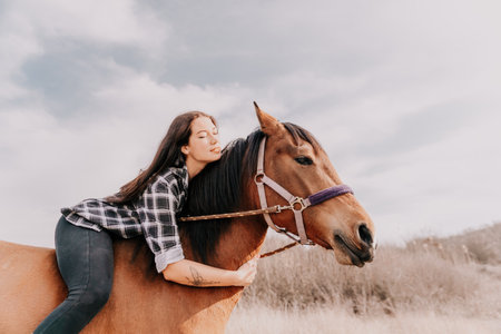 Young happy woman in hat with her horse in evening sunset light. Outdoor photography with fashion model girl. Lifestyle mood. Concept of outdoor riding, sports and recreation.の写真素材