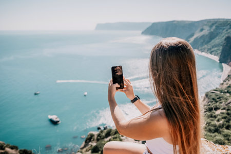 Digital nomad, woman in the hat, a business woman with a laptop sits on the rocks by the sea during...