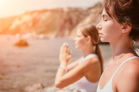 Woman sea yoga. Happy women meditating in yoga pose on the beach, ocean and rock mountains. Motivation and inspirational fit and exercising. Healthy lifestyle outdoors in nature, fitness concept.の写真素材