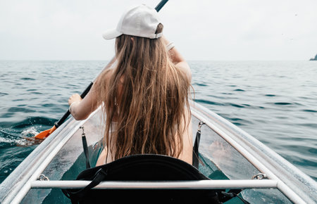 Woman in kayak back view. Happy young woman with long hair floating in transparent kayak on the crystal clear sea. Summer holiday vacation and cheerful female people relaxing having fun on the boatの写真素材