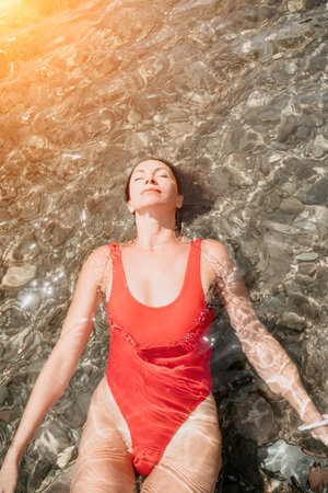 Woman travel portrait. Close-up portrait of a happy woman with long hair in a red bikini, floating in water and smiling at the camera.の写真素材