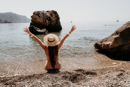 Woman travel sea. Happy tourist in hat enjoy taking picture outdoors for memories. Woman traveler posing on the beach at sea surrounded by volcanic mountains, sharing travel adventure journeyの写真素材